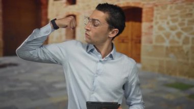 İspanyol gözlüklü bir adam eski şehirde tabletle kollarını esnetiyor. Saat takıyor. Etrafı kırsal mimari ve klasik atmosferle çevrili..