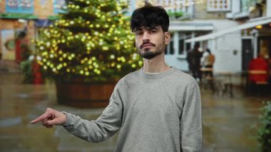 Şehirdeki bir sokakta genç bir adam açık havada aydınlık bir noel ağacını işaret ediyor..