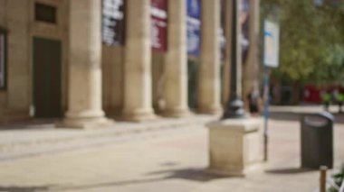 Güneşli bir günde arka planda tarihi mimari sütunların yanından yürüyen, aydınlık ve gölgeli insanların olduğu şehir manzarası