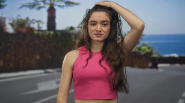 Pembe ekili bluzlu kadın öğleden sonra güneşli sahil caddesinde parmaklarını saçlarında gezdirir; gerginlik.