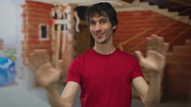 Genç adam yarı yapılı, tuğladan duvarları açık, kırmızı gömlekli ve sırıtan bir binanın içinde el çırpıyor. Mutluluk..