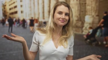 Eski bir şehir caddesinde arka planda yürüyen bulanık insanlarla gülümseyen bir kadın şehir yaşamını ve sarışın saçlarını gösteriyor..