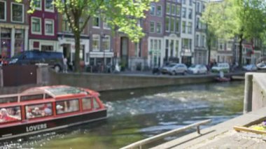 Kanal boyunca park halindeki bisikletlerin, ağaçların ve geleneksel Hollandalı evlerin yer aldığı bulanık kentsel manzaralı Amsterdam Kanalları Hollanda 'da dağılmış, canlı bir şehir manzarası yaratıyor..