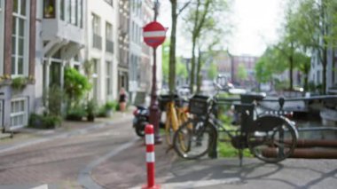 Bisikletli Ambu Kanalı 'nın bulanık görüntüsü, yürüyen kadın, ağaçlar ve tipik Hollanda mimarisi, ilkbaharda sakin bir şehir manzarası yaratıyor..