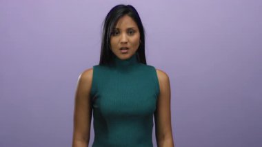 Mor bir duvarın önünde şaşkınlığını ifade eden, yeşil bir bluz giyen, dışlanmış bir arkaplan ile samimi bir an sergileyen, duygularını vurgulayan bir kadın..