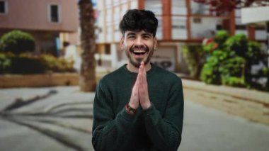 Neşeli bir suratı olan genç adam güneşli bir günde ağaçların ve binaların olduğu bir şehirde eğleniyor..