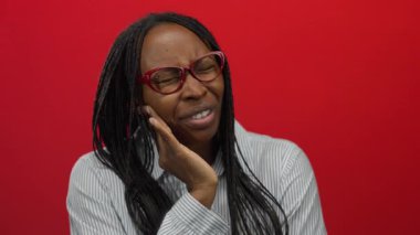 Kırmızı duvara karşı gözlük takan dişleri ağrıyan bir kadın ellerinin yanağında duygularını gösteriyor..