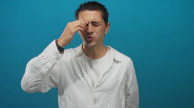 Beyaz gömlekli genç adam mavi arka plana burnunu sokuyor. Hayal kırıklığı ya da rahatsızlık veriyor..