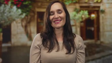 Çevresindeki taş duvarlar ve yeşilliklerle çevrili açık havada gülümseyen ve öpüşen bir kadın, arka planda doğa olan neşeli bir anı yakalıyor..