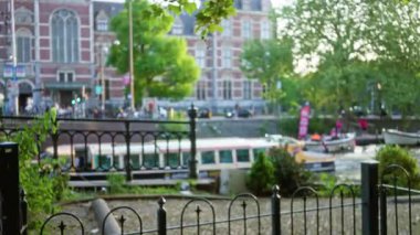 Amsterdam 'daki teknelerin ve tarihi binaların bulunduğu bulanık kanal manzarası insanların yaşadığı canlı bir şehir akşam manzarası sergiliyor..