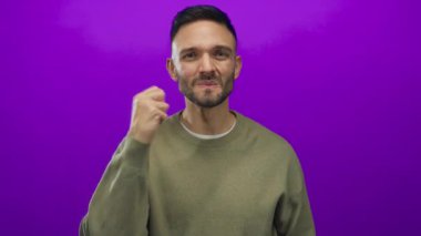 İspanyol genç adam elleri ile canlı bir mor arka plan karşı, ifade edici bir poz sergileyen stüdyo ışıkları altında yeşil bir eşofman altı giyerek.