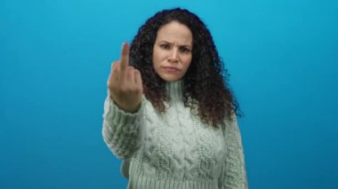 Öfkesini el hareketleriyle ifade eden bir kadın canlı mavi bir arka plana karşı kazak giyiyor..