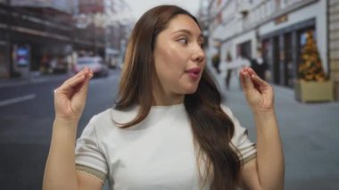 Hareketli şehir caddesinde elleri ile hareket eden beyaz tişört giyen genç İspanyol kadın; hareketli sohbet.