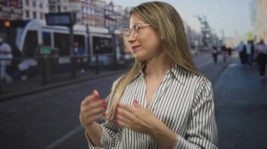 Tramvay durağının yakınındaki işlek bir şehir sokağında açık avuçlar gösteren sarışın kadın; açıklık.