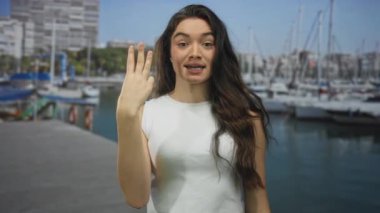 İspanyol kadın, liman iskelesinde demirli bir teknenin yanında üç parmağını göstererek gülümsüyor..