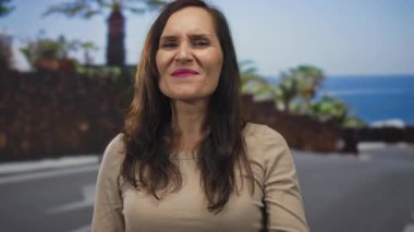 Gülümseyen genç İspanyol kadın, güneşli sahil geçidinde kaya boynuzlarıyla el kaldırıyor..