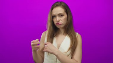 Beyaz bluz giyen, parlak ışıklar altında mor stüdyoda saçlarına dokunan beyaz saçlı, genç, esmer kadın..