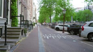 Avrupa 'da kaldırım taşı, park edilmiş arabalar ve dağılmış yeşilliklerle bulanık şehir manzarası bulutlu bir günde sakin bir bokeh etkisi yakalıyor.