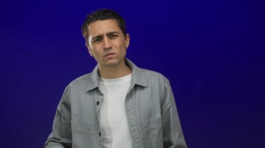 Mavi arka planda ciddi şekilde düşünen genç bir adam derin derin düşünüyor ve düşünceli giyiniyor izole edilmiş ve odaklanmış bir şekilde bir anlık yansıma gösteriyor..