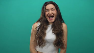 Genç İspanyol kadın sırıtır sırıtır sırıtır sırıtır dişlerini deniz mavisi stüdyosunun arka planına karşı; sevinç güveni.