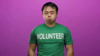 Yeşil gönüllü gömlekli genç adam neşeli pembe arka plana karşı komik bir yüz ifadesi sergiliyor.