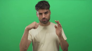 Genç İspanyol adam, basit yeşil stüdyo duvarına sıkılmış yumruğuyla yumruk atıyor. Kararlılık..