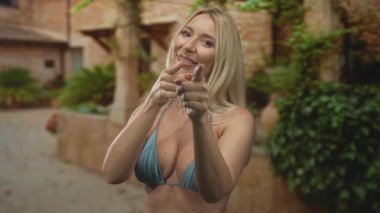 Kadın dekoltesini açtı ve kamerayı eski şehir sokağındaki taş binaya doğrulttu..