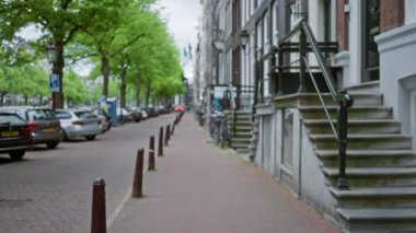 Park halindeki arabaları ve klasik mimarisi olan Amsterdam caddesinin bulanık görüntüsü, Hollanda 'da sakin bir şehir manzarası sergiliyor..