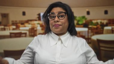 Artı, zarif beyaz tişörtlü, rahat restoranda rahat bir şekilde poz veren, kendine güveni ve arkadaş canlısı tavırları olan, boyunda bir kadın..