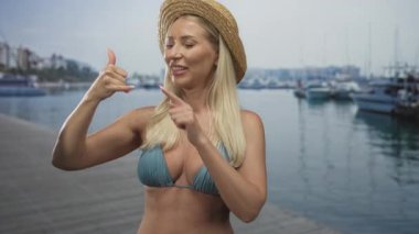 Saman güneş şapkası takan ve yeşil bikinili bir kadın limandaki rıhtımlı tekneleri inşa ederek ve yanında oynayarak bir jest yapıyor..