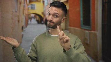 Genç bir adam, eski bir şehir kasabasında, renkli dar bir sokakta el kol hareketi yapıyor, parmaklarıyla olumsuzluğu ifade ederken, dışarıda canlı bir İspanyol kentinde elini uzatıyor..