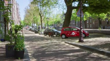 Avrupai şehirde bulutlu bir öğleden sonra manzarası açık gökyüzünün altında park halindeki arabaları, ağaçları ve kentsel yolları gösteriyor, sakin bir açık hava atmosferini somutlaştırıyor.