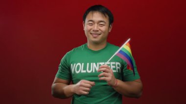 Elinde gökkuşağı bayrağı tutan ve kırmızı duvarın önünde barış işareti yapan genç adam Igbt toplumuna gurur ve destek gösteriyor..