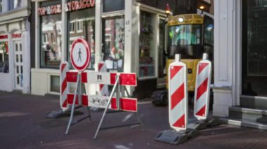 Bir tütün dükkanının önünde kalın kırmızı ve beyaz çizgili inşaat bariyerlerinin sokak manzarası, kentsel açık havada çözülmüş bokeh etkisi ve endüstriyel ekipmanların yer aldığı.