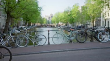 Bisikletler, bulanık yeşil ağaçlar ve parlak gün ışığı altında tarihi mimarinin yer aldığı bulanık amfi sahnesinde bir kanal boyunca dizildi..