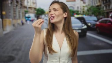 Beyaz kolsuz bluzlu genç bir kadın güneşli bir şehir caddesinde havaya bir öpücük yolluyor..