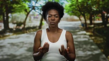 Kadın, huzurlu park ortamında el hareketleriyle para, açık havada finans ve ifade taşımacılığı, doğal güzellik ve etkileşim sergiliyor..