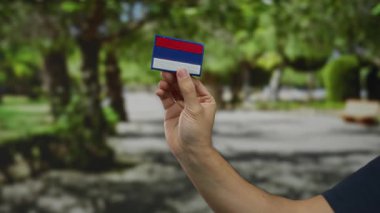 Güneşli bir park ortamında Rus bayrağı taşıyan bir adam beyaz bir el ve bulanık doğal arka planı olan renkli nakışlar sergiliyor..