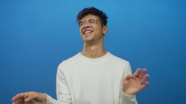 Stüdyoda gülümserken işaret eden gözlüklü İspanyol adam canlı mavi arka plana karşı; neşe.