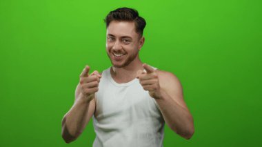 Sakallı genç adam, sağlam yeşil duvara karşı güvenle gülümsüyor ve tezahürat ve pozitiflik öneriyor..