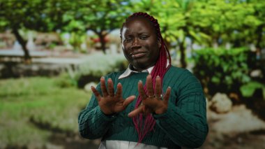 Kırmızı örgülü Afro-Amerikalı bir kadın parkta yeşil bir kazak giyip doğal ortamda duygularını ifade ederek reddediyor..