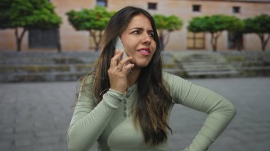 Açık havada akıllı telefondan konuşan, karışık duygular besleyen, yeşillikli bir şehirde yaşayan bir kadın..