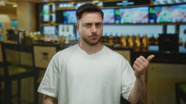 Sakallı genç adam, bir restoranın barında modern iç tasarım ve günlük atmosfer sergileyerek mizahi bir şekilde işaret ediyor..