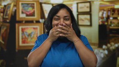 Çerçevelenmiş tablolar ve sergi duvarlarındaki sanat eserleriyle dolu bir binada kadın elleri ile ağzını kapatıyor..