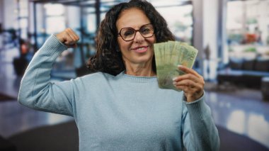 Otel resepsiyonundaki kadın, elinde Arjantin pezolarıyla banknotları idare etmede ve iş ortamında parayı gülümseyerek idare etmede güven ve başarı gösteriyor..