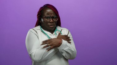 Beyaz önlüklü, steteskoplu, izole edilmiş mor arka planda titreyen Afrikalı Amerikalı kadın..