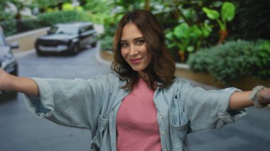 Etrafı yeşilliklerle çevrili bir caddede neşeli bir şekilde gülümseyen kollarını açmış İspanyol bir kadın ve açık bir gökyüzü altında şehirli mutluluğu ve canlılığını somutlaştıran arabalar..