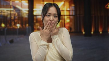 Genç Çinli bir kadın geceleri kameraya öpücük yolluyor. Arka planda renkli ışıklar var. Mutluluk ve bağlarını ifade ediyor..