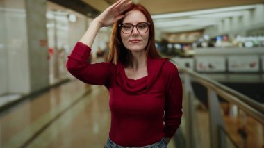 Alışveriş merkezinde gülümseyen bir kadın canlı ışıklandırmayla yakalandı. Kızıl saçlı, genç, yetişkin, gündelik giyinmiş, mutluluk ve güven saçıyor..