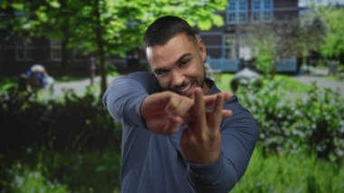 Gülümseyen ve hashtag sembolü oluşturan adam, güneşli yeşil parktaki binanın yakınındaki elleri ile; oyunculuk bağlantısı.